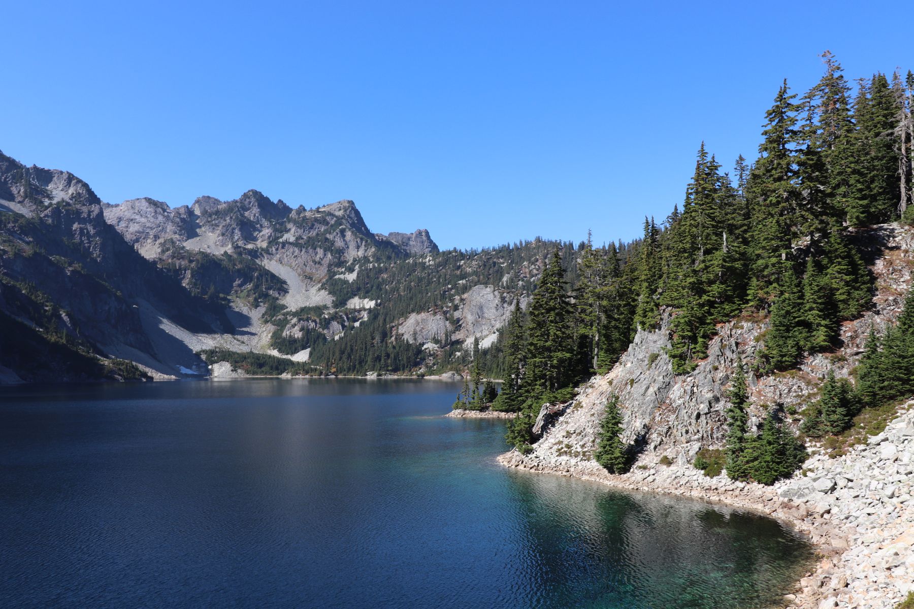 A deep blue alpine lake below granite cliffs and firs