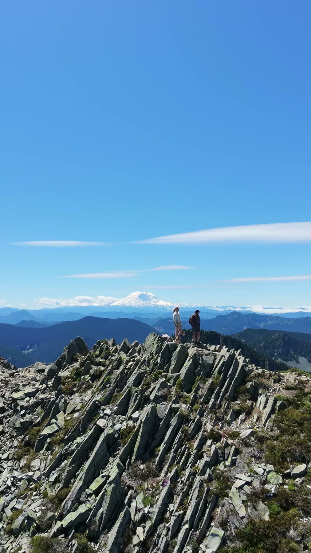 Aerial view of hikers on a rocky summit, Mount Rainier on the horizon