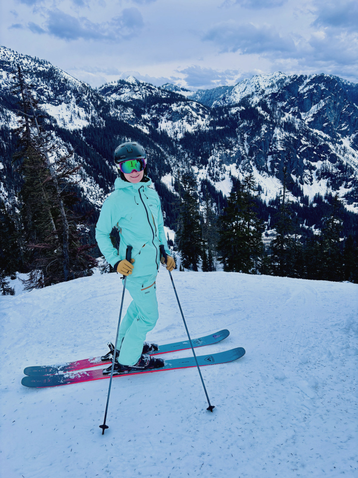 Ari in a teal suit on a ridge above snowy peaks