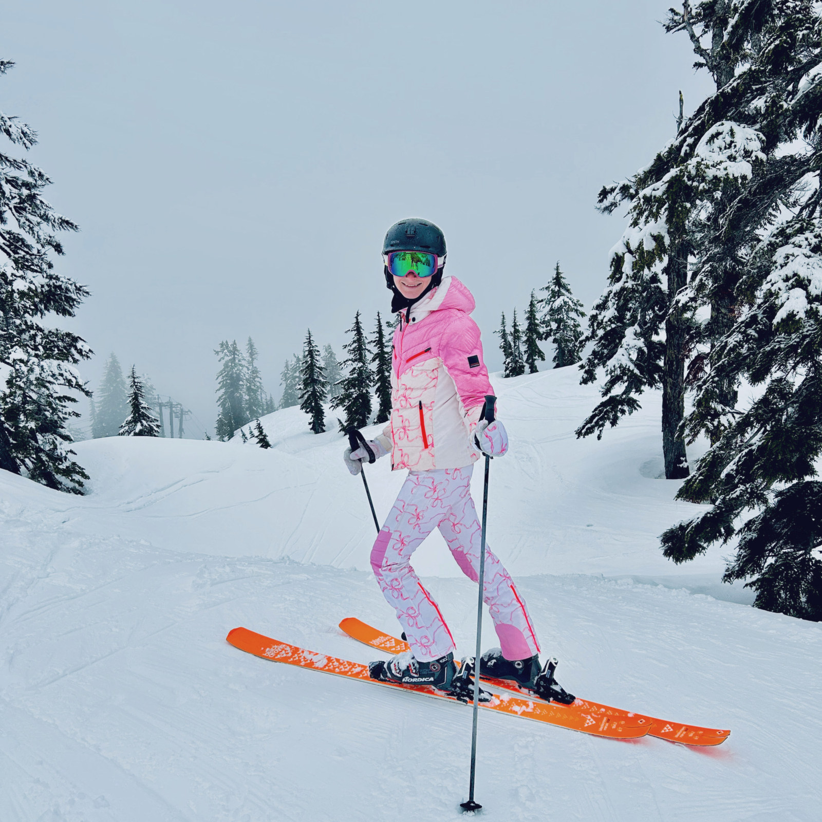 Ari in pink on a groomer between snow-laden firs