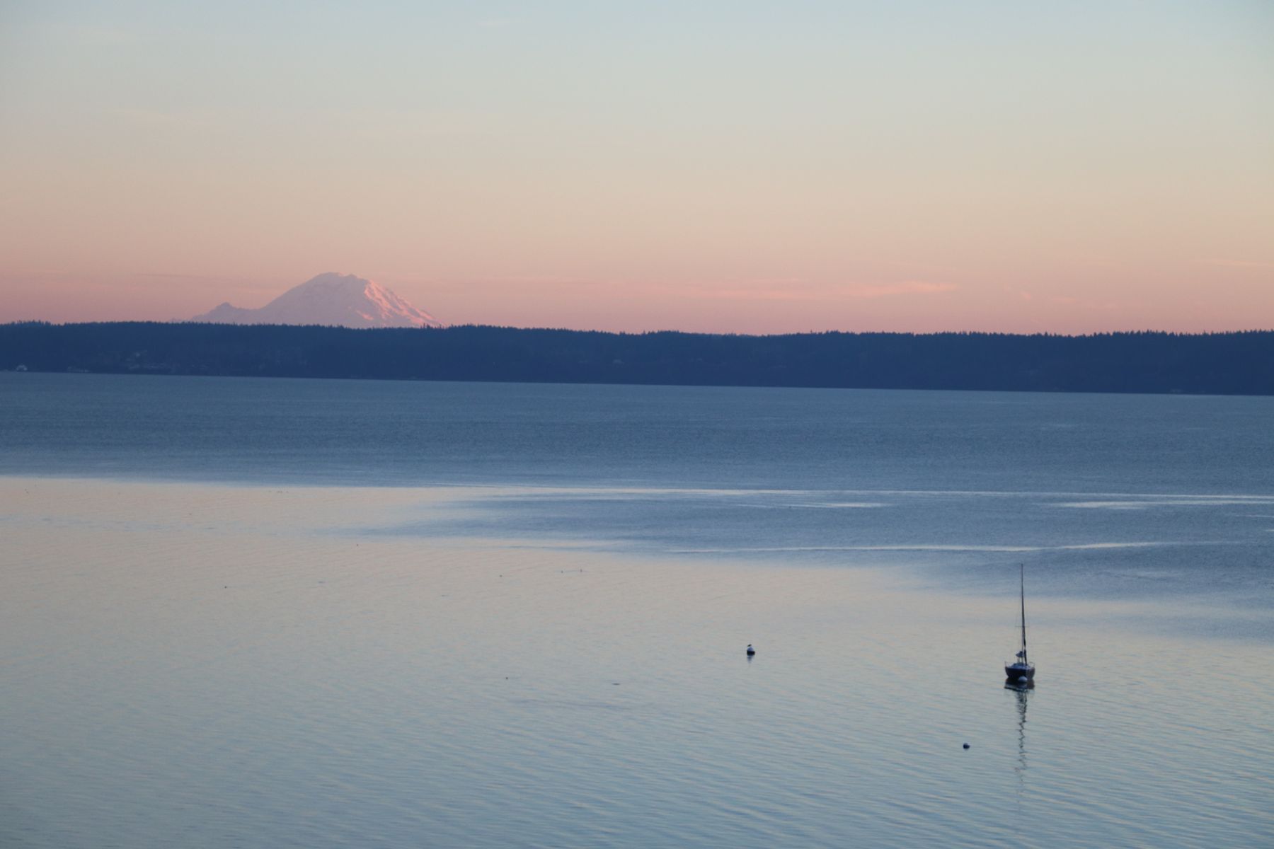A sailboat on still water at sunset, a mountain on the horizon